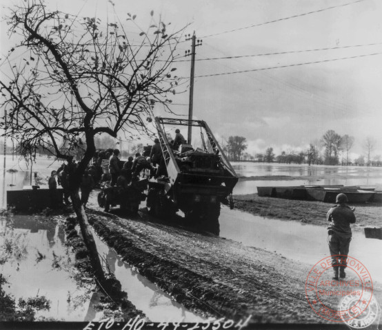 Dans un paysage innondé, suite au débordement de la Moselle, un détachement du génie US apporte des barques d'assaut dont certaines se trouvent déjà sur la terre ferme. Sur l'un des camions, on peut distinguer une jeep