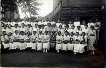 [Groupe de jeunes filles posant devant leur pensionnat avec des écharpes et des paniers fleuris vers 1910]