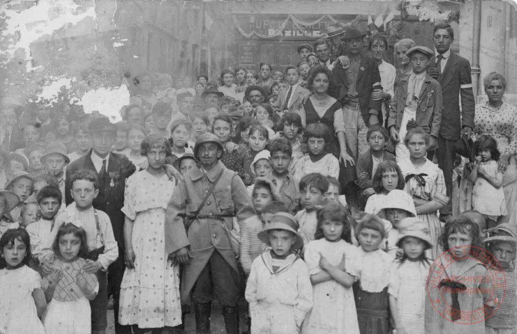 Groupe de personnes posant avec un soldat français, plusieurs d'entre elles portent un brassard blanc
