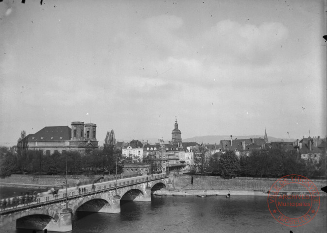 [L'entrée de ville depuis le pont. L'église Saint-Maximin, le Beffroi, l'Hôtel de Ville et le tramway]