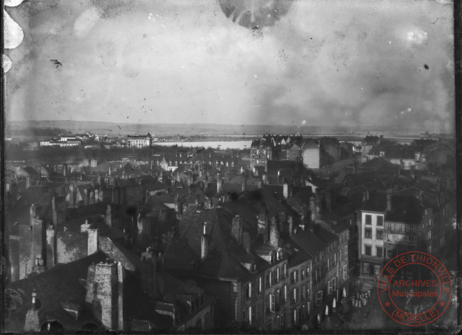 [Vue panoramique de Thionville prise depuis le Beffroi vers 1910. Premier plan, la place du Marché, puis l'hôpital Sainte-Elisabeth et le Niederfield. Au fond les près du Niederfield inondés]