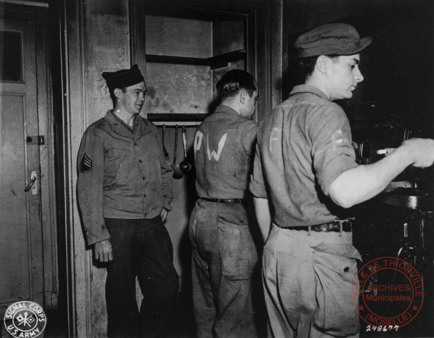 Le sergent Joseph T. Marlin surveille deux prisonniers de guerre allemands qui préparent le déjeuner. Thionville, janvier 1945