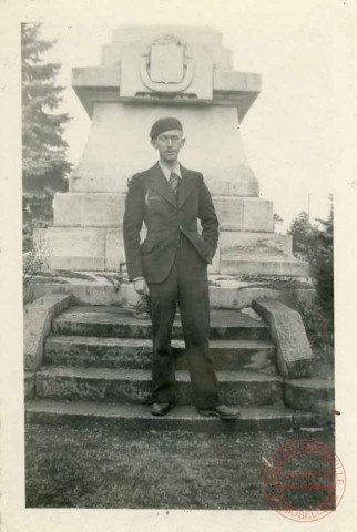 Portrait d'un homme en béret posant devant une stèle ou monument aux morts