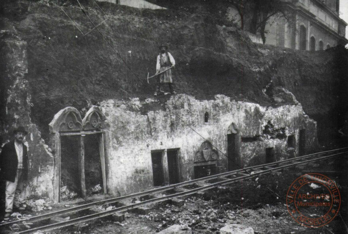 Le démantèlement des fortifications de Thionville 1902-1903. Découverte du quartier médiéval de Thionville entre l'église Saint-Maximin et la Moselle lors des travaux de démolition des fortifications. Ici une façade XIIIe (la porte) avec des éléments du XIVe (les fenêtres). Notons que le niveau médiéval fait beaucoup plus bas que l'actuel niveau de la ville. Ce quartier fut enterré, à partir du XVe siècle pour assurer un puissant rempart sur la Moselle 1902.