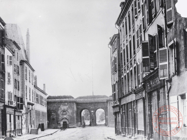 [La porte du Pont prise depuis la place du Marché et différents commerces, Flosse, B. Mayer]