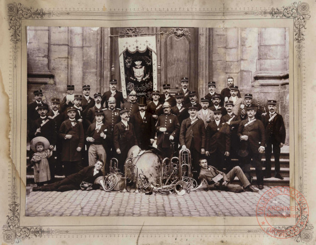 [Photo de groupe de la société philharmonique de Thionville devant l'église Saint-Maximin, il est écrit 1868 sur la bannière]