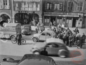 [Scène de vie place du Marché. Rassemblement de personnes autour d'une Citroën 2CV. On peut y voir la quincaillerie P. Breistroff et sa camionnette ainsi que la Brasserie du Commerce]