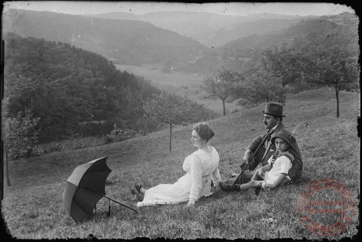 [Des parents avec leur enfant assis dans l'herbe sur une colline]