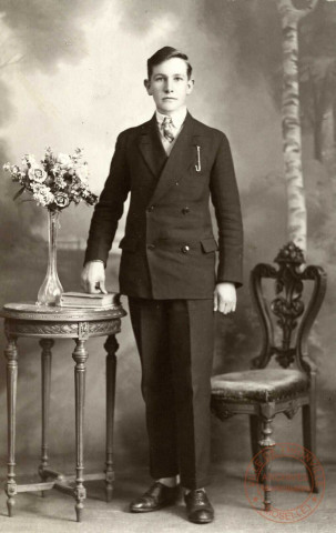 [Portrait d'un jeune homme en costume foncé posant le poing sur un livre fermé]