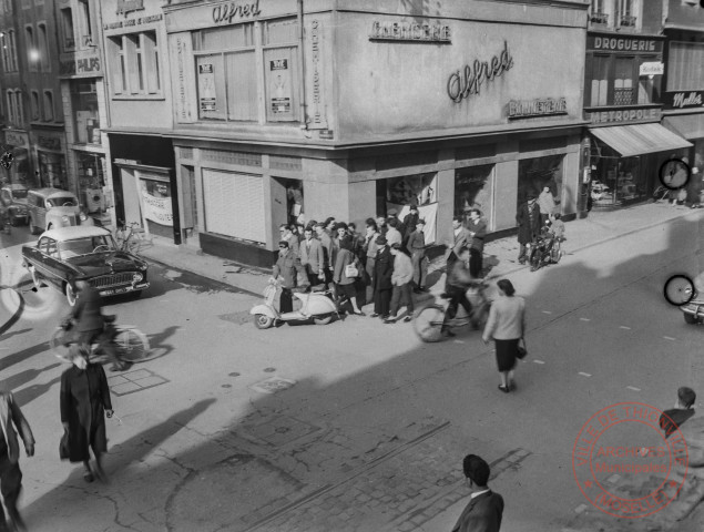 [Scène de vie à l'angle de la place du Marché et de la rue du Mersch. On y voit la chemiserie-bonneterie Alfred, la droguerie métropole]