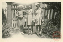 3 jeunes filles en chapeau posent dans la cour d'une maison