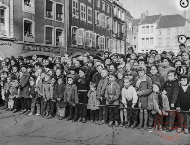 [Groupe d'enfants et de famille attendant derrière une barrière place du Marché]