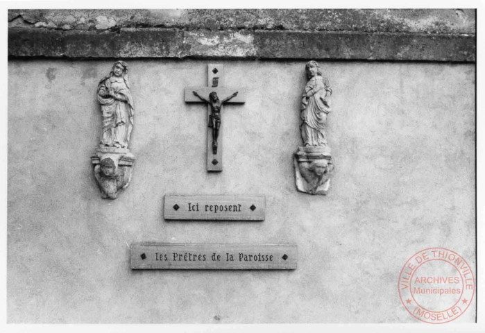 Statuettes de la Vierge et Saint-Jean de chaque côté de la croix, accrochée sur le mur de l'église paroissiale Saint-Rémy de Puttelange-lès-Thionville. Sous chaque statuette des têtes d'angelots
