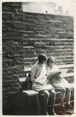 2 petites filles lisent un livre assises sur un banc