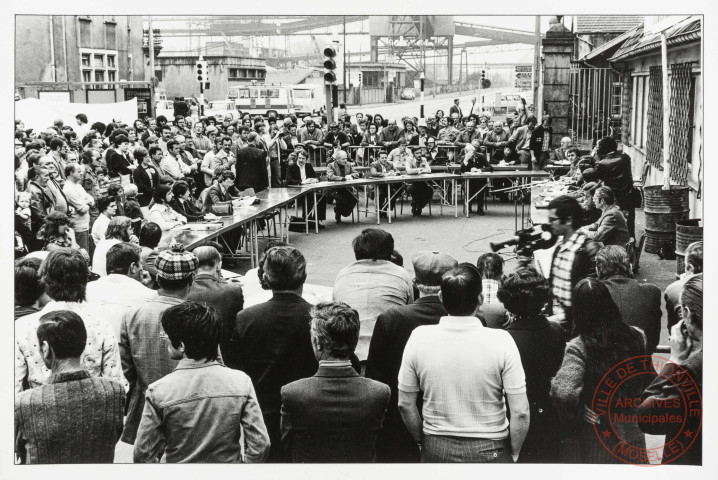 [Manifestation de protestation contre la fermeture des hauts-fourneaux de Thionville. Rassemblement autour conseil municipal avec la pancarte placée au-dessus d'eux "Thionville doit vivre"]