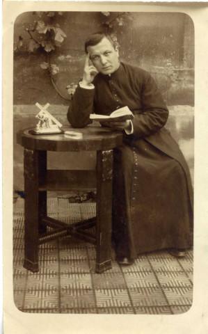 [Photographie d'un prêtre attablé avec un livre à la main en 1915]