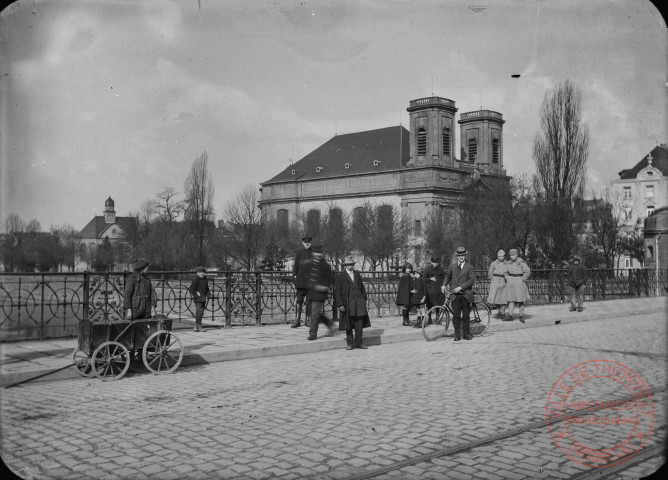 [L'entrée de ville depuis le pont. L'église Saint-Maximin, le Beffroi, l'Hôtel de Ville et le tramway]