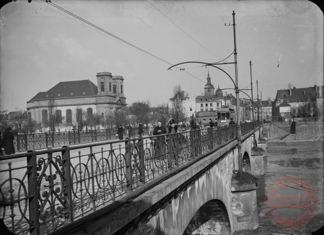 [L'entrée de ville depuis le pont. L'église Saint-Maximin, le Beffroi, l'Hôtel de Ville et le tramway]