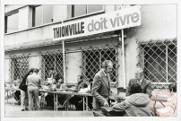 [Manifestation de protestation contre la fermeture des hauts-fourneaux de Thionville. Rassemblement autour conseil municipal avec la pancarte placée au-dessus d'eux "Thionville doit vivre"]