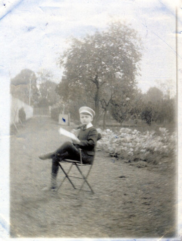 [Photographie d'un jeune garçon assis sur une chaise, en uniforme d'écolier, dans un jardin en 1914]