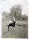 [Photographie d'un jeune garçon assis sur une chaise, en uniforme d'écolier, dans un jardin en 1914]