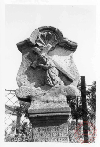 Bildstock situé à l'angle de la rue de Trèves et la route de Rodemack à Fixem. Croix érigée en 1769 (date portée sur le fût) pour Anne Tindingers. Portement de croix, calice, fleur de lys, feuillage, fleur