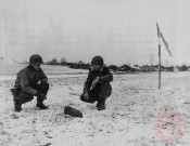 Lieutenant Henry C. Laner (à gauche) Headquarters Div. Artillery et le Lieutenant Donald P. Brown du 3rd Armered Field Artillery du Xxe Corps US examinent un obus de 155mm trouvé à Bousse, le 21 janvier 1945