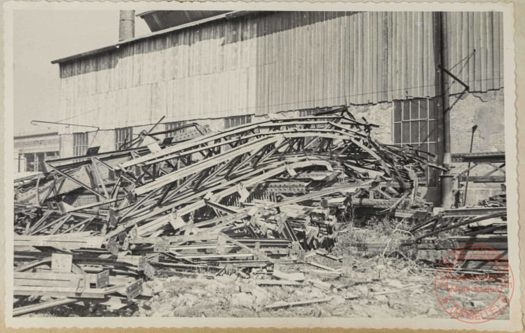 Atelier basique. On voit le derrière du bâtiment et le mur du côté sud. Les bombes ont cisaillé et tordu les charpentes entreposées là par les allemands. Lorsque la photo a été prise, les dégâts causés au bâtiment étaient déjà réparés.